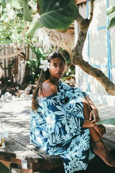 a woman sitting on a wooden bench wearing a blue dress and flower in her hair