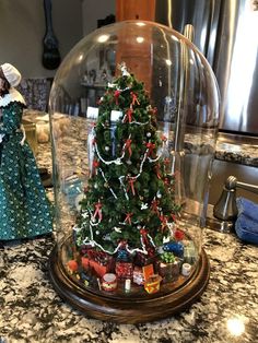 a christmas tree under a glass dome on top of a kitchen counter next to a doll