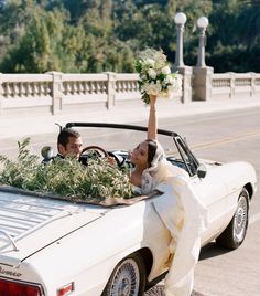 a bride and groom sitting in the back of a convertible car with greenery on top