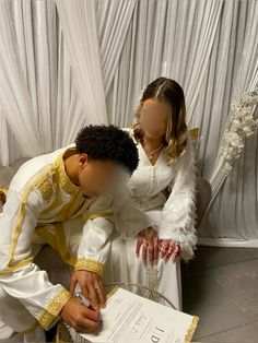 two people dressed in white and gold, one is signing something on a piece of paper