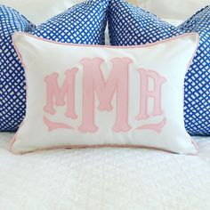 two blue and white pillows with pink monogrammed letters on them, sitting on a bed