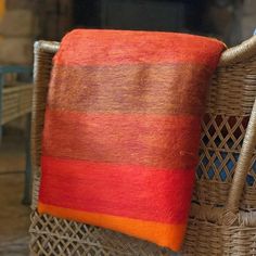 an orange and red blanket sitting on top of a wicker chair next to a fire place