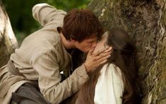 a man kissing a woman on the cheek next to a tree