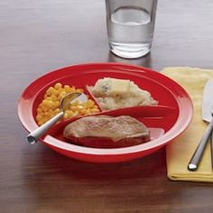 a red plate topped with meat and veggies next to a glass of water