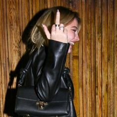 a woman in black leather jacket holding up her hand and making the middle finger sign