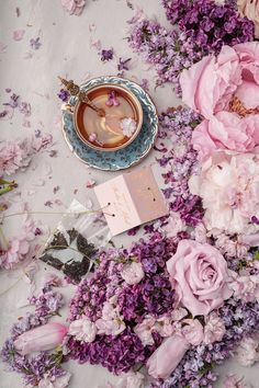 a cup of tea and some pink flowers on a white tablecloth with a blue saucer