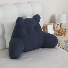 a blue teddy bear sitting on top of a bed next to a night stand and lamp