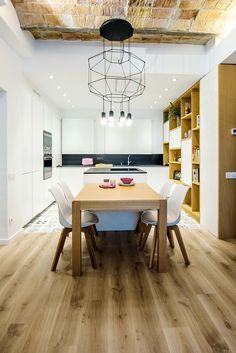 a dining room table with white chairs in front of an open kitchen