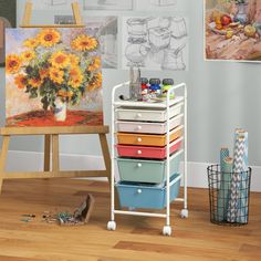 an easel filled with lots of drawers next to a painting and other art supplies