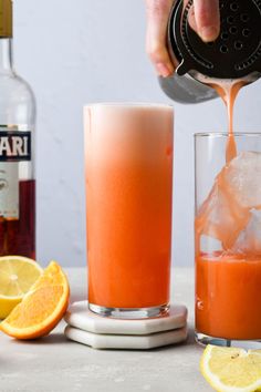 someone pouring orange juice into a glass with ice and lemons next to the bottles