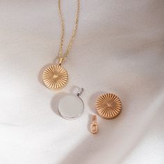 two pieces of jewelry sitting on top of a white sheet next to a gold chain