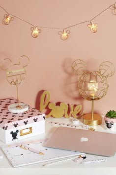 a desk topped with a laptop computer next to a mouse head and love sign on top of a pink wall