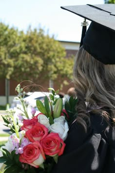 a woman wearing a graduation gown and holding a bouquet of flowers