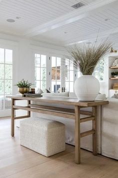 a white vase sitting on top of a wooden table next to a bench in a living room