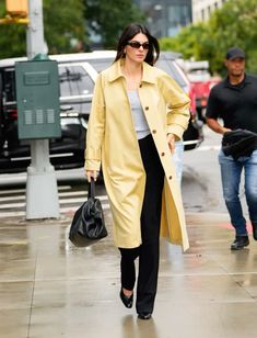 a woman in a yellow trench coat is walking down the street