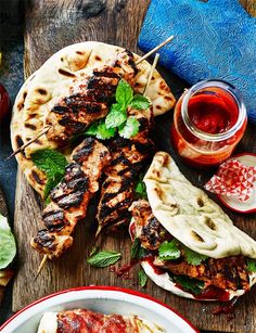 grilled chicken skewers and pita breads on a cutting board with dipping sauce