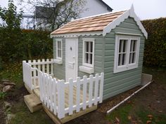 a small green house with a white picket fence