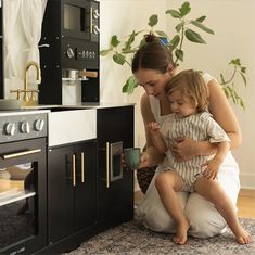 a woman kneeling down next to a child in front of an oven