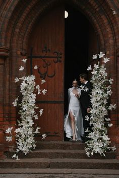 a bride and groom standing in front of a doorway with white flowers on the steps