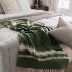 a green and white blanket laying on top of a bed next to two pillows in front of a window