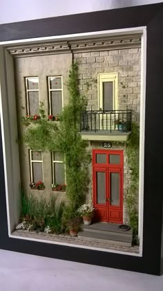 a small model of a house with red doors and windows on the outside, surrounded by greenery