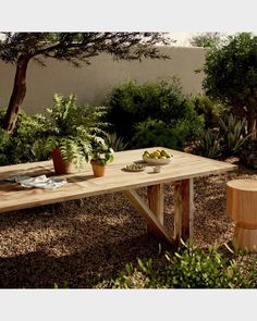 a wooden bench sitting in the middle of a garden next to trees and bushes with potted plants on it