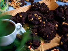 chocolate cookies and nuts on a wooden cutting board next to a cup of green tea