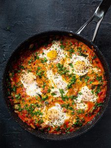 an iron skillet filled with eggs and tomato sauce on top of a black surface