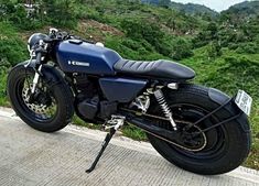 a blue motorcycle parked on the side of a road next to a lush green hillside