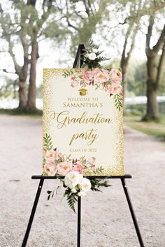 a sign that is sitting on top of a tripod with flowers and greenery