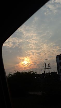 the sun is setting over some buildings and power lines as seen through a car window