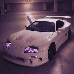 a white sports car parked in a parking lot at night with its hood up and lights on