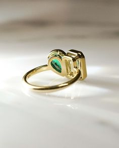 a gold ring with a green heart on the front and side, sitting on a white surface