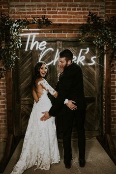 a bride and groom standing in front of a brick wall with the words the cheers written on it