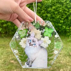 a hand holding a glass ornament with a cat on it's face