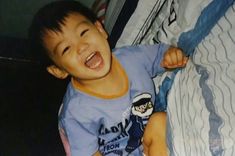 a young boy is laughing while laying on a bed with his arm around the pillow