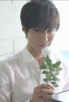 a person holding a flower in their hand and looking at the camera man is wearing a white shirt