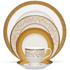 the gold and white dinnerware is set with an ornate design on it's side