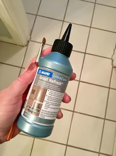 a person holding a paintbrush in their hand near a tile floor and wall with white grout on it