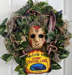 a wreath that has a mask on it and some leaves around the edges, with a sign reading welcome to camp crystal lake