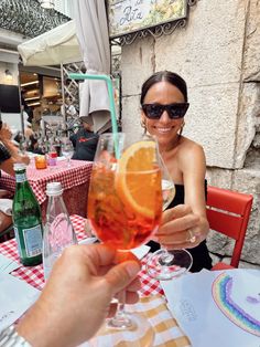 a woman sitting at a table holding up a wine glass with an orange slice in it