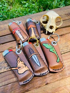 four leather keychains with different designs on them sitting on a wooden table next to a skull