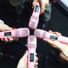 four pink microphones are arranged in the middle of a circle with hands holding them