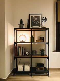 a book shelf with glass vases and other items on it in front of a white wall