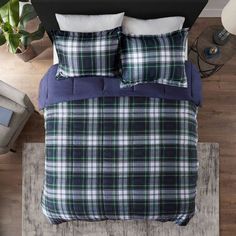 a bed with blue and green plaid comforter on top of wooden flooring next to a plant