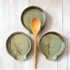 three green dishes with wooden spoons in them on a white wood tableclothed surface