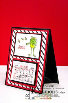 a card with a calendar on it and a frog in the middle, sitting next to a red background