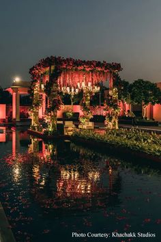 an outdoor wedding venue is lit up with pink flowers and greenery on the water