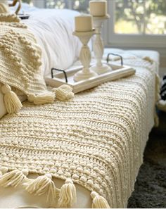 a white crocheted blanket on top of a bed next to a candle holder