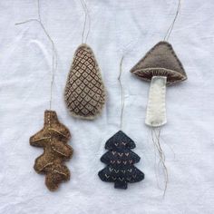 three ornaments are hanging from twine strings on a white surface, one has a mushroom and the other is a christmas tree